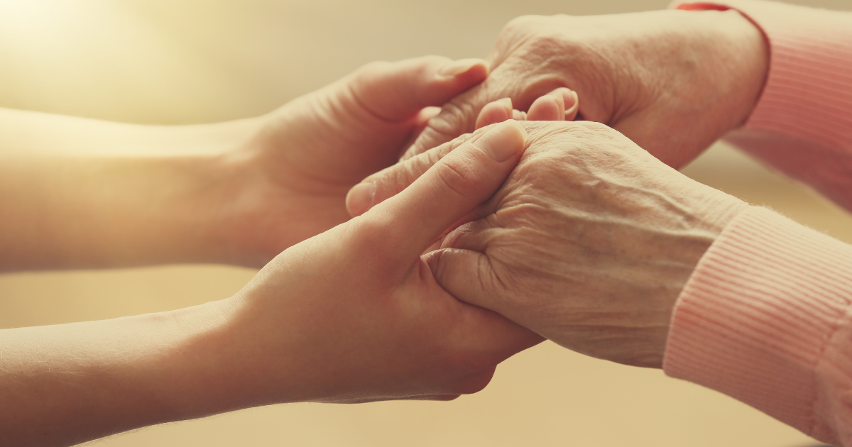 A caregiver holds hands with a senior, displaying empathy and concern, qualities agencies look for when hiring caregivers.