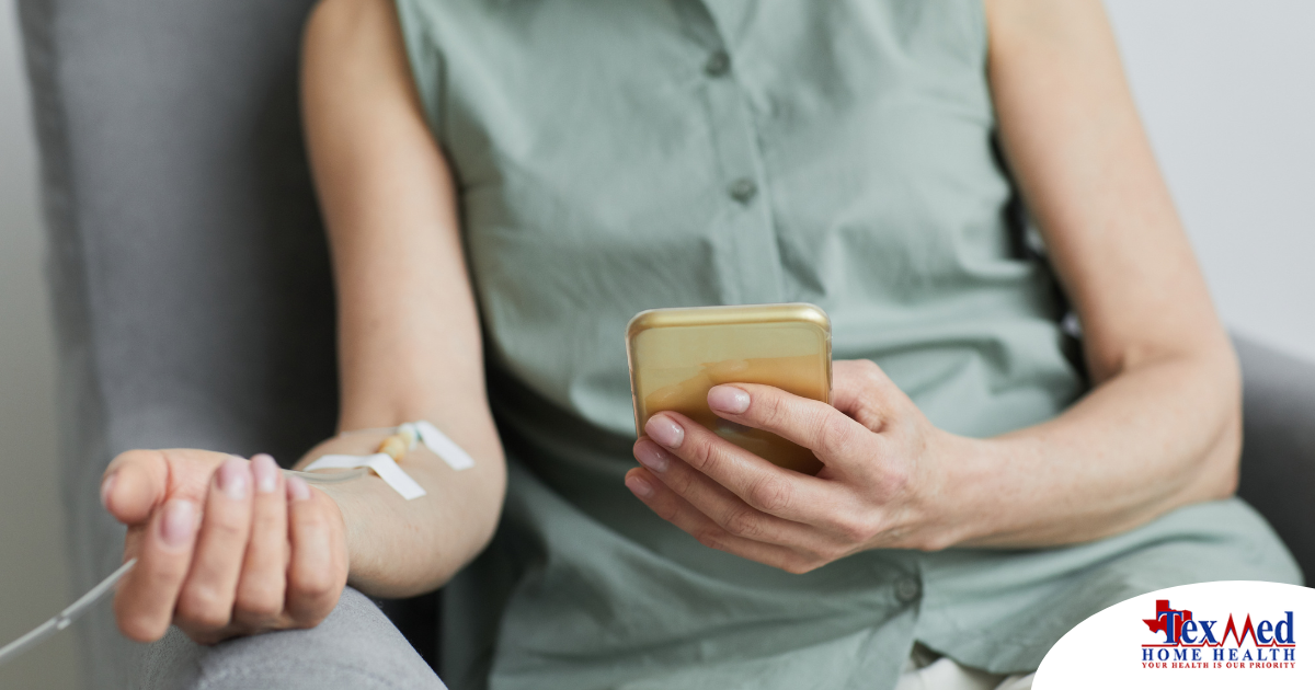 A woman comfortably receives IV therapy at home while using her phone.