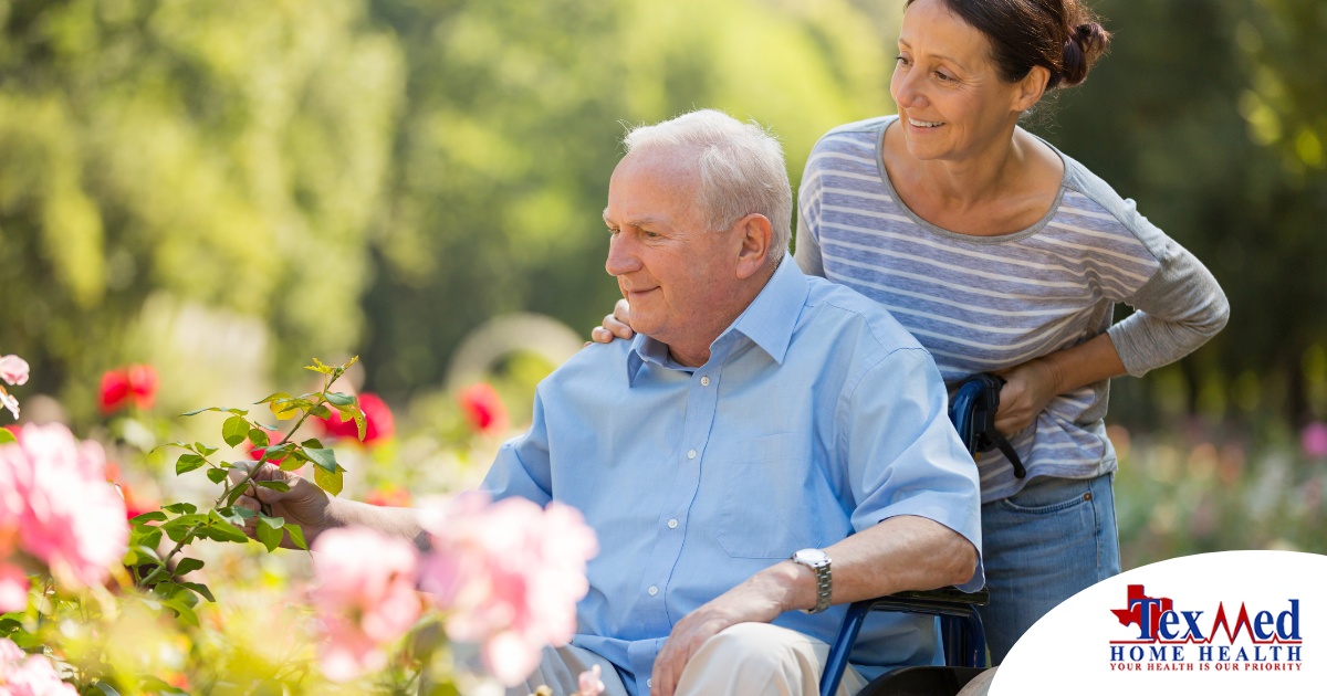 A caregiver brings an older adult with a wheelchair to see some flowers representing how professional caregivers can make outdoor activities accessible.