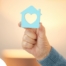 A hand holds up a cutout of a home with a heart in it, representing the home care industry.