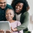 A daughter looks at a tablet with her older parents, representing technology and how ti can help with aging in place.