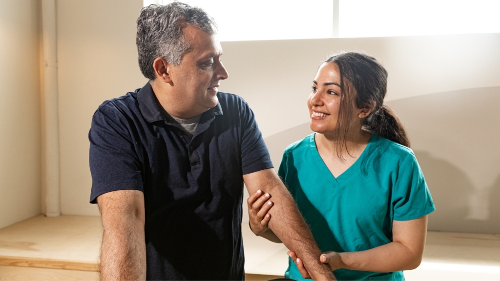 A young female caregiver with a warm and supportive expression assists an elderly man using a walker. She provides physical and emotional support as he walks, demonstrating compassionate skilled nursing care in a home setting.