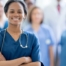 A woman in scrubs with a healthcare team behind her represents starting a new home health care job with a confident approach.