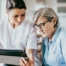 A nurse helps an older patient by showing her a tablet representing the role of tech in registered nurses’ roles in care.