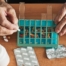 Older hands organize pills into a pill organizer, showing a great tool for managing medications.