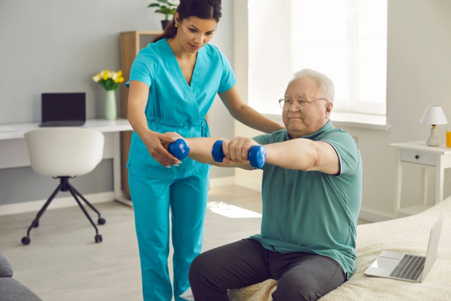 Occupational Therapy in Temple, TX – Therapist Assisting Senior with Strength Exercises Occupational therapist helping a senior man perform arm exercises with dumbbells during occupational therapy in Temple, TX.